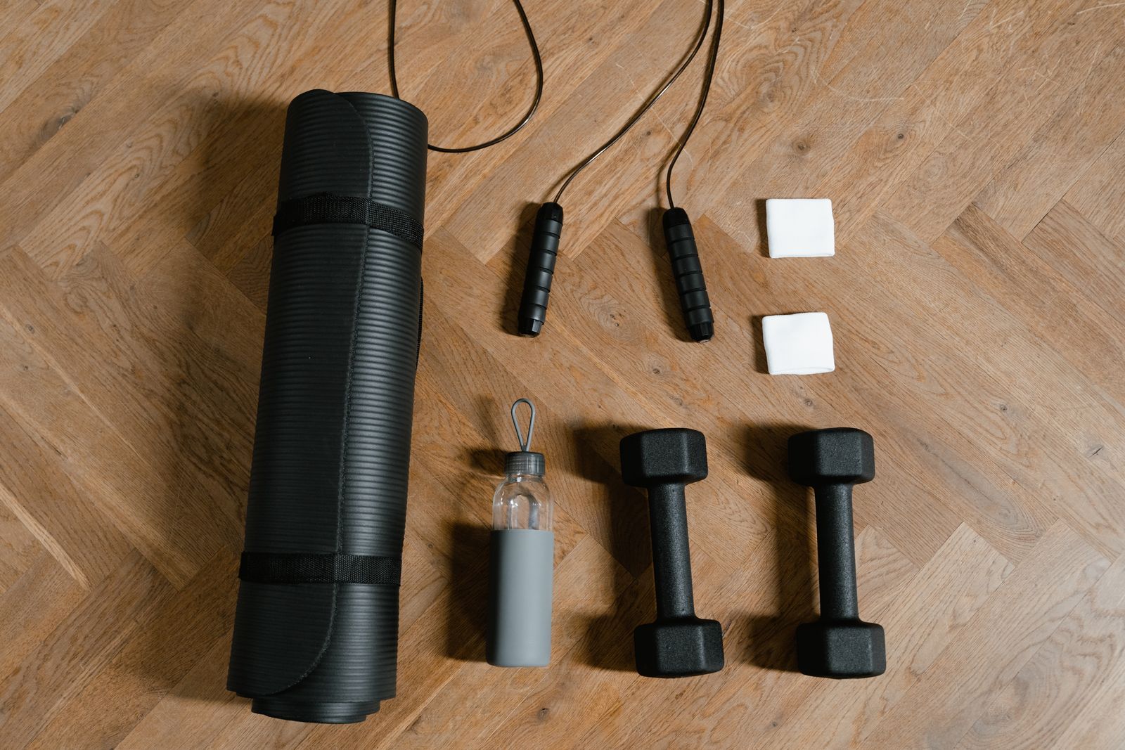 Ahşap zeminde yoga matı, dambıllar ve atlama ipi
