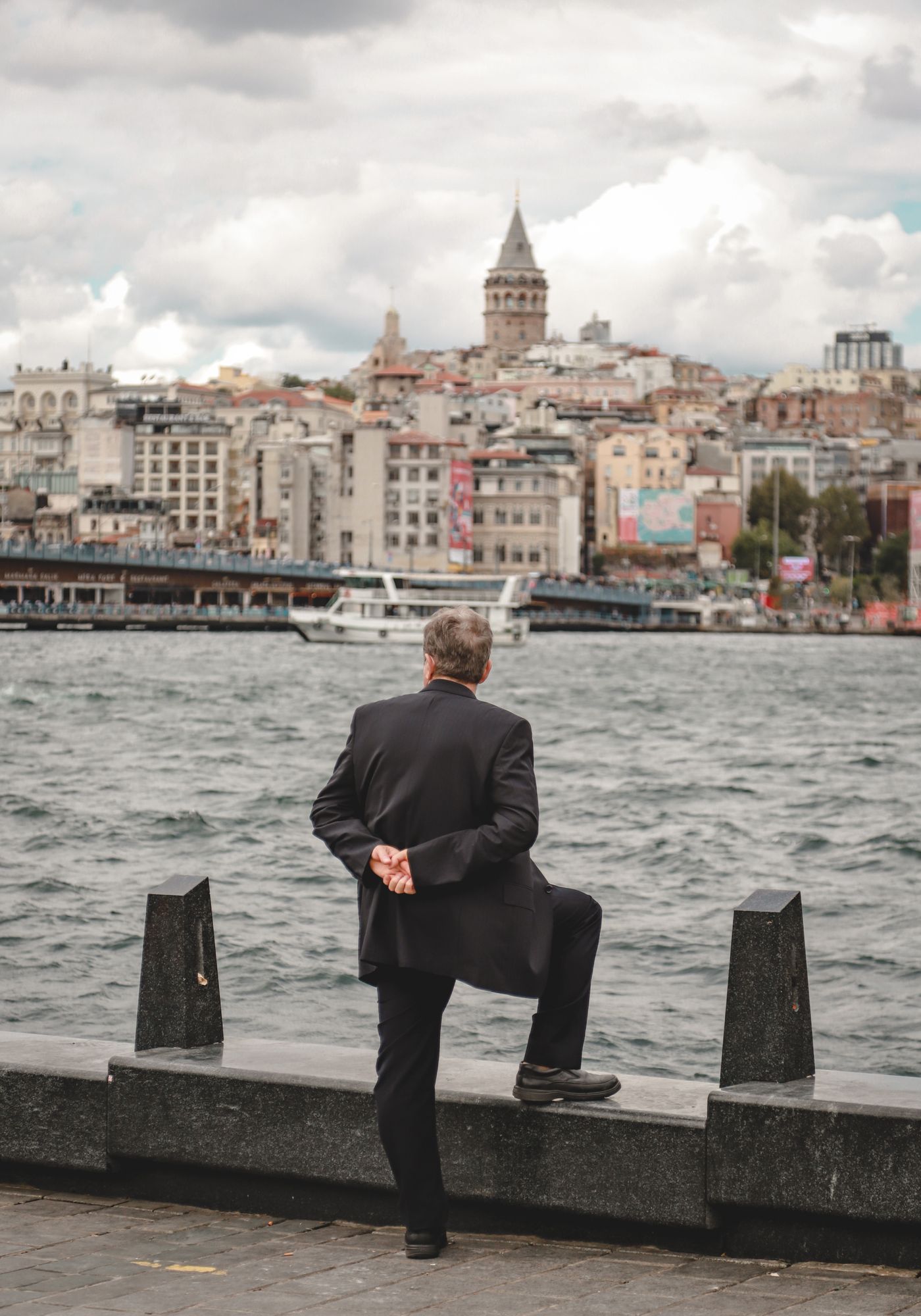 Kıyıda durup karşıdaki Galata'ya bakan takım elbiseli bir adam, arkadan
