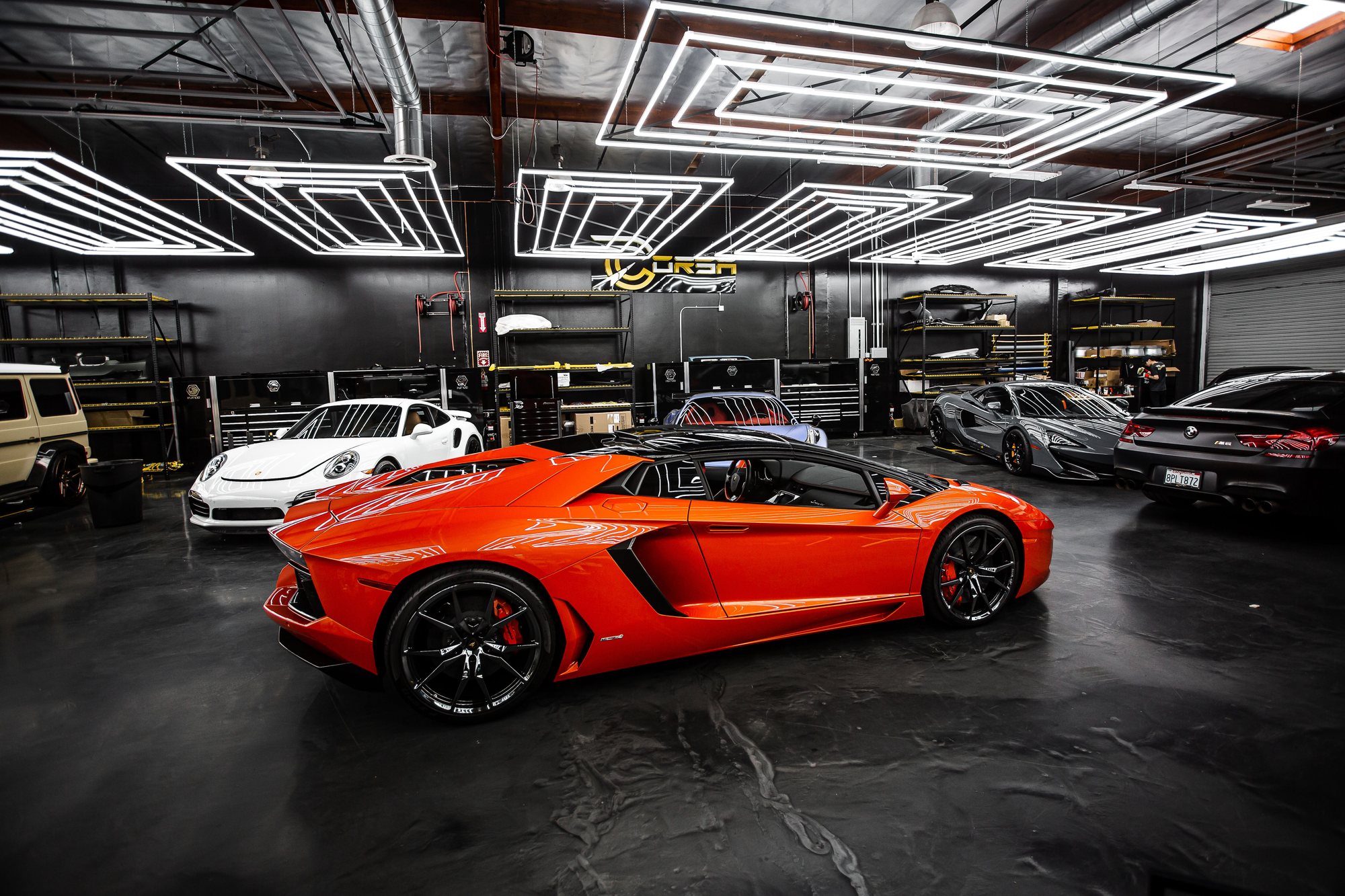 Altıgen ışıklı tavanın altında turuncu bir spor araba, koyu bir detailing stüdyosu